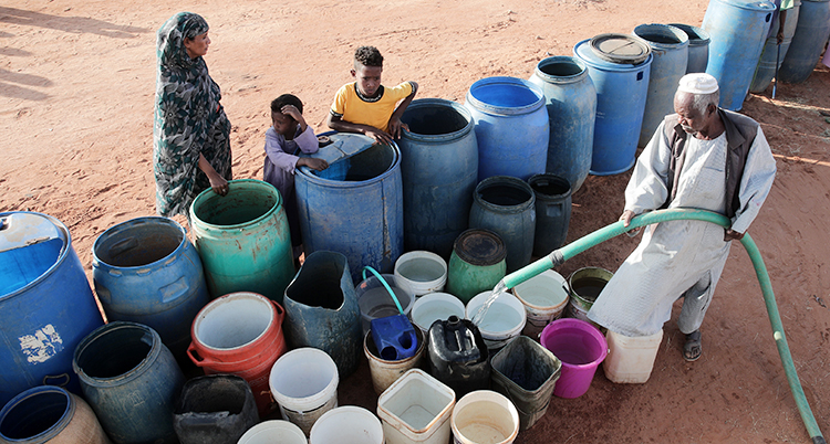 En man fyller tunnor och hinkar med vatten. En kvinna och två barn tittar på.