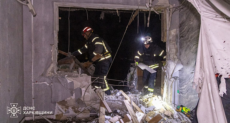 Två brandmän står i ett trasigt hus.