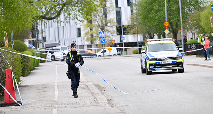 Uppsala. En polis står på trottoaren. En polisbil står på gatan.