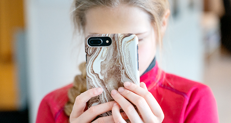 En blond flicka håller en mobiltelefon framför sitt ansikte.
