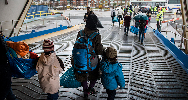 Många personer går i land från en stor färja. Närmast syns en mamma som håller ett barn i handen.