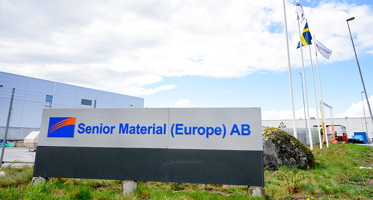 En skylt där det står Senior Material Europa AB. I bakgrunden syns en fabrik.
