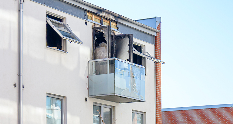 Ett hus med lägenheter. En balkong är skadad av brand.