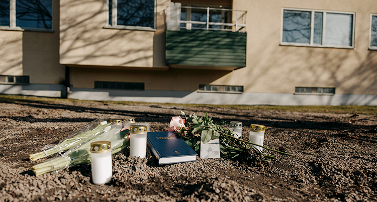 Blommor och ljus som ligger på marken utanför ett hus med lägenheter.