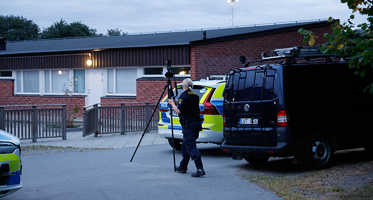 En polis bär en kamera. Två av deras bilar är parkerade brevid skolan.