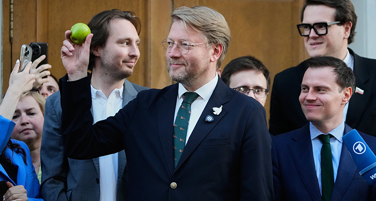 Han har kostym och han håller i ett äpple.