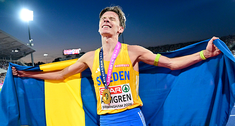 Han håller en svensk flagga bakom ryggen. Han har en medalj runt halsen.