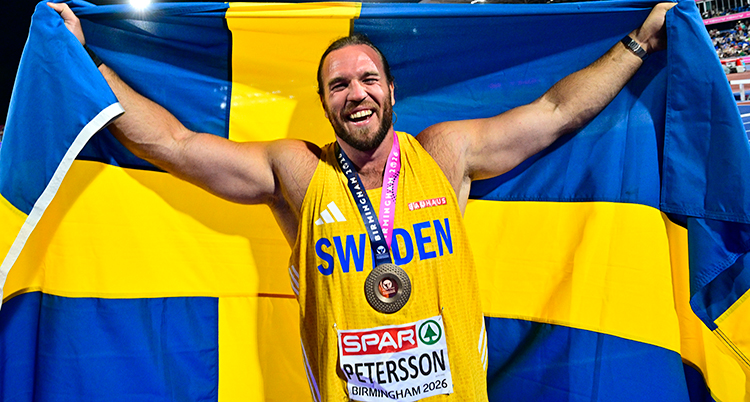 Han har en medalj runt halsen. Han håller i en svensk flagga. Han är glad.