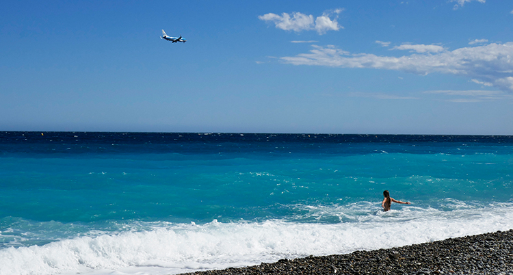 En person badar på en strand. På himlen syns ett flygplan.