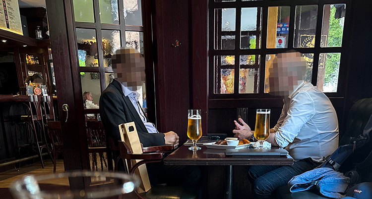 Två personer sitte rvid ett bord på en restaurang. Ansiktena är pixlade.