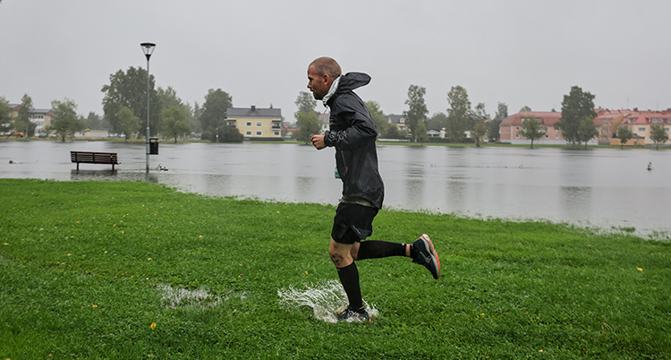 En man joggar på en blöt gräsmatta. Marken intill är översvämmad.