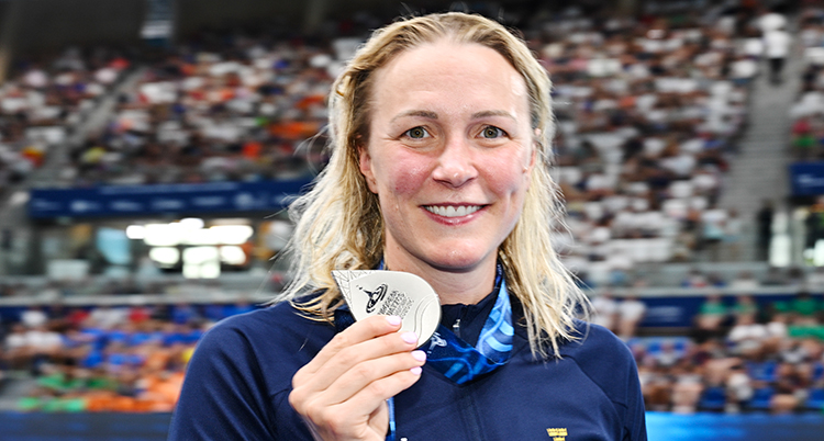 Hon håller upp medaljen. Hon är glad.
