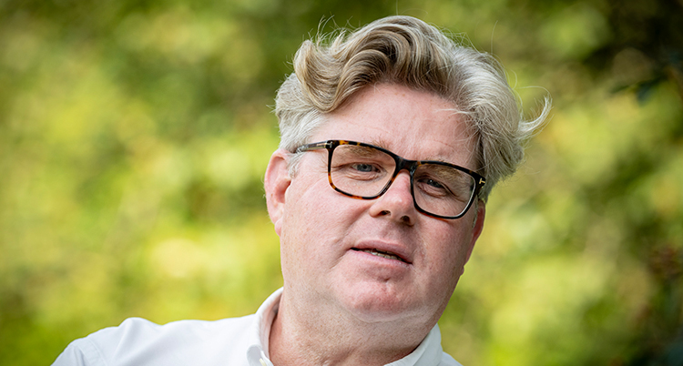 Han har vågigt grått hår och glasögon.