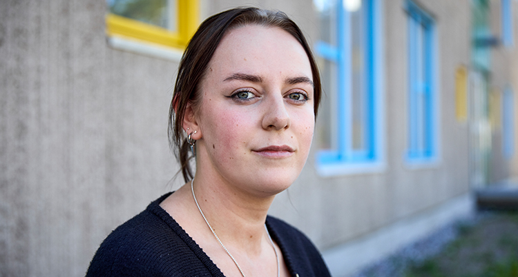 Ett porträtt. Hon står mot en vägg vid ett hus.