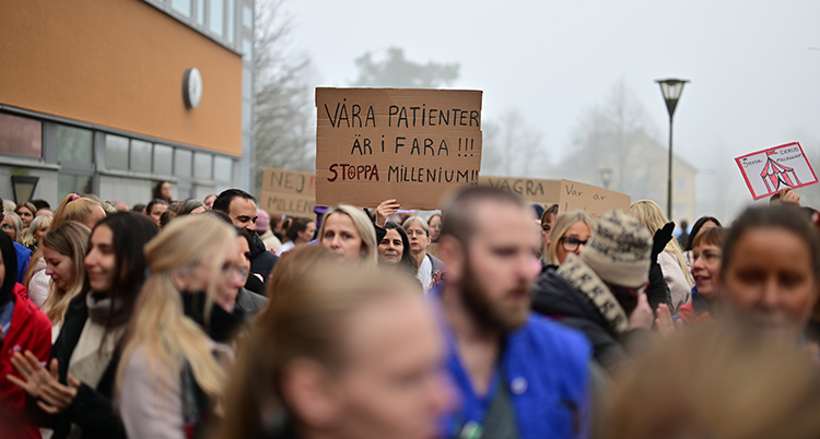 Folk är samlade utanför en byggnad. Några håller upp skyltar.