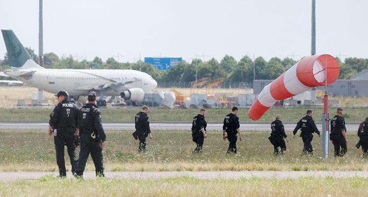 Ungefär tio poliser går på ett fält. I bakgrunden syns ett flygplan som står på marken.