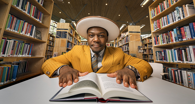 Han sitter i ett bibliotek med en bok framför sig.