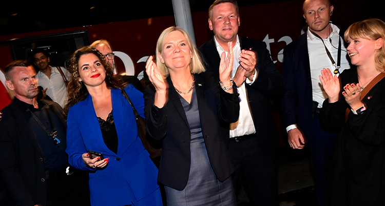 Hon står mellan flera andra personer och klappar i händerna.