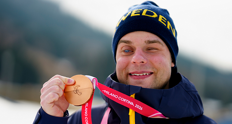 Han håller fram en medalj. Han är glad.