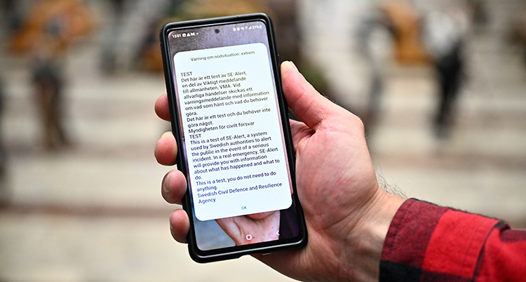En hand håller i en mobil. Ett meddelande med mycket text syns på skärmen. Test står det högst upp i meddelandet.
