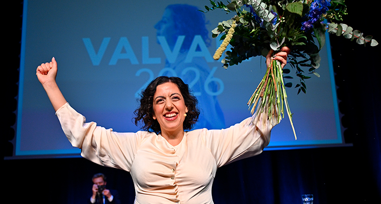 Hon håller ut armarna. Hon har en blomsterbukett i ena handen. Hon är glad.