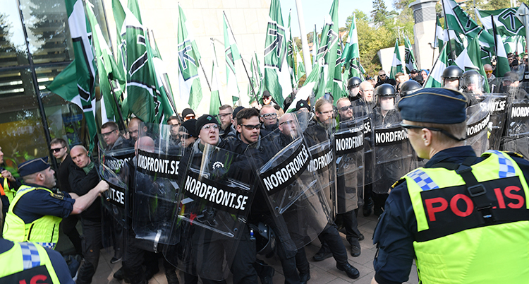 Personer som demonstrerar. De har sköldar av plast. Poliser är där.