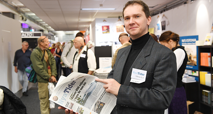 Han står på Bokmässan och håller i ett nummer av tidningen Nya Tider.