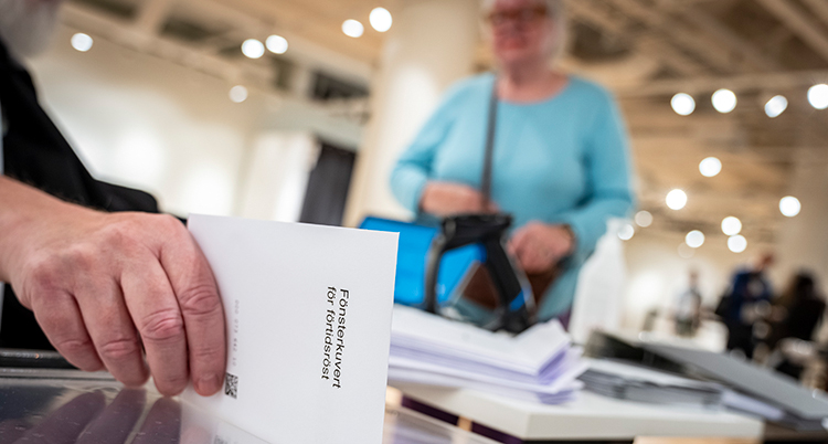 En person står framför röstmottagaren som lägger valkuvert i urnan.