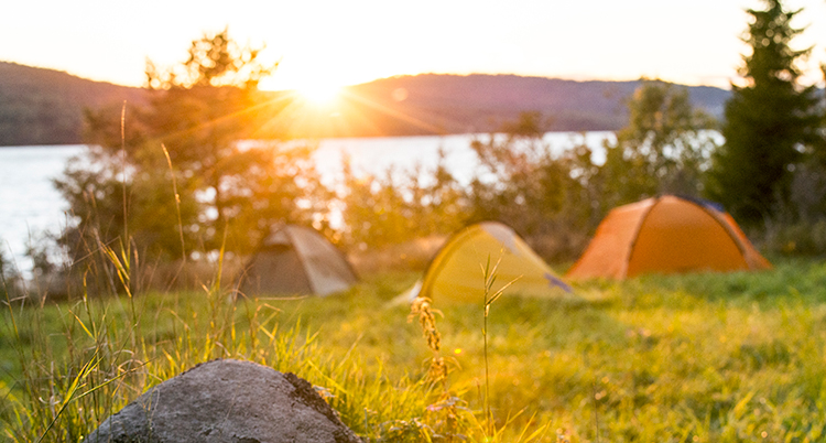 Tält på en kulle med utsikt över en solnedgång och vatten.