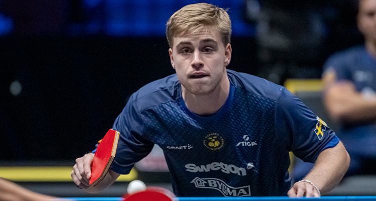 Han spelar bordtennis. Han håller i ett racket och tittar på bollen.