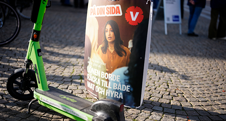 En bild med reklam för Vänsterpartiet som sitter på en stolpe på en gata.