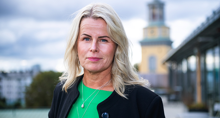 Hon tittar in i kameran. I bakgrund syns en suddig stad.