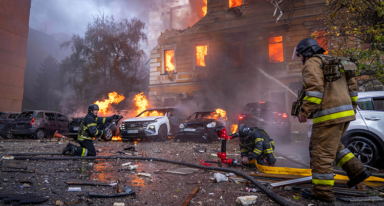 Brandmän sprutar vatten mot huset. Det brinner ur fönstren. Förstörda bilar brinner också.