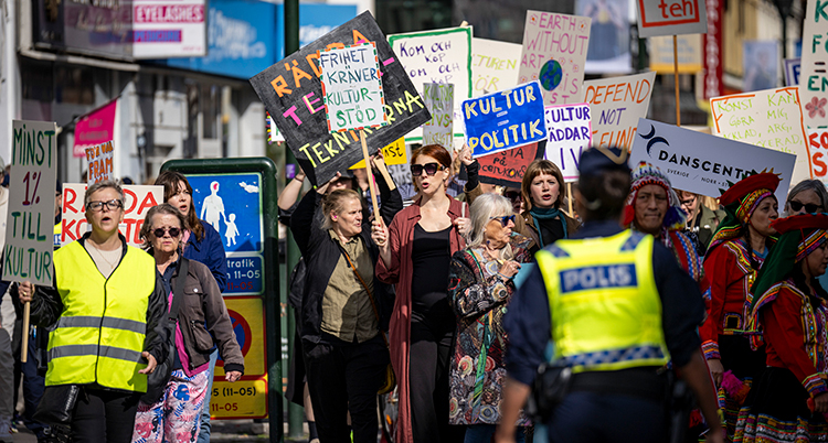Folk håller upp skyltar med olika budskap om kultur. En polis följer protesterna.