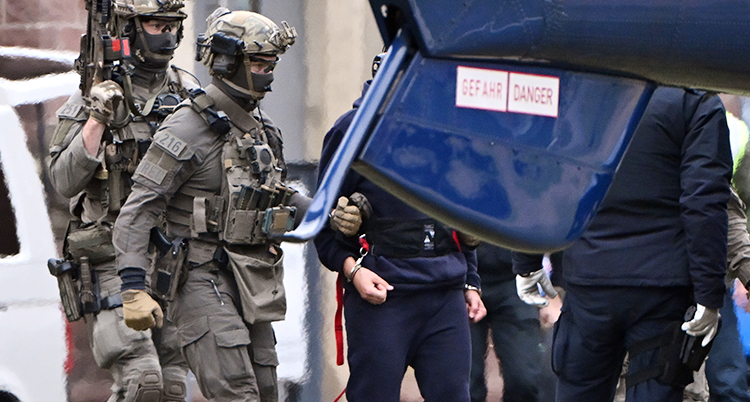 Poliser med vapen och gröna kläder leder en man som har fått handklovar. Vi ser inte mannens ansikte.