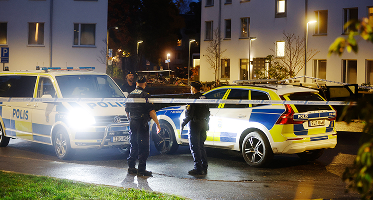 Poliser och polisbilar bakom tejp som poliserna har satt upp för att spärra av området.