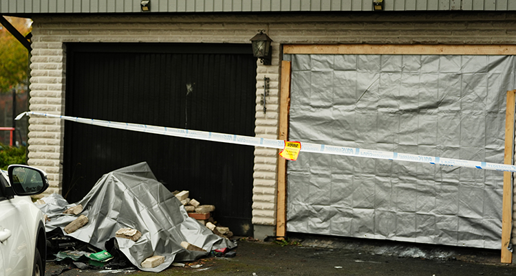 Ett garage med två portar. Ena porten är täckt med plast. Poliserna band finns framför garaget.