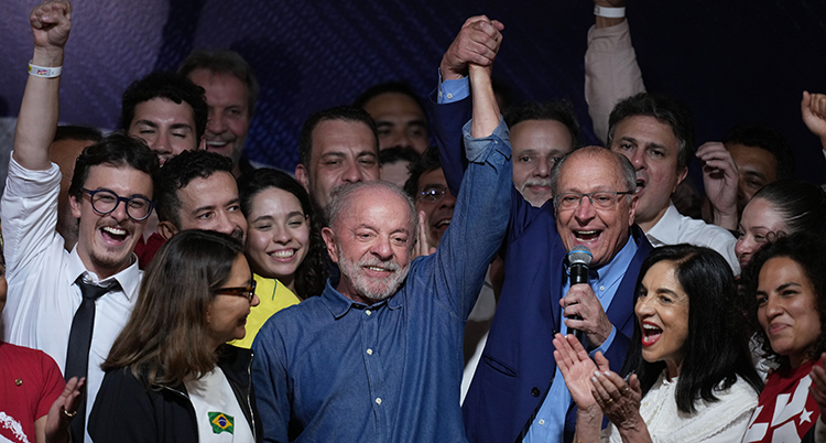 Massor av glada människor står runt Lula da Silva som sträcker upp en arm i luften.