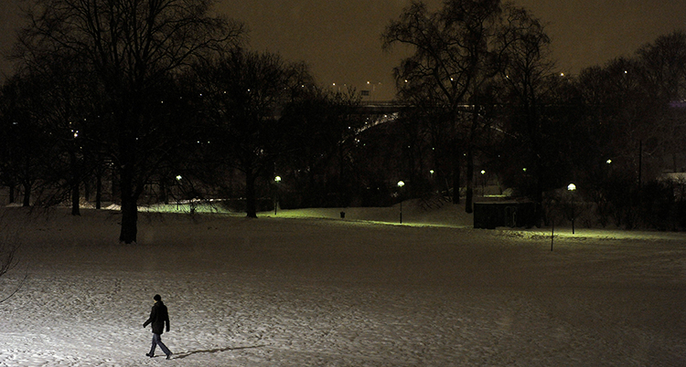 En person går genom en park. Det är mörkt ute.