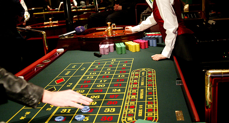 En person lägger spelmarker på några siffror på ett bord. Längre bort snurrar hjulet för roulette.